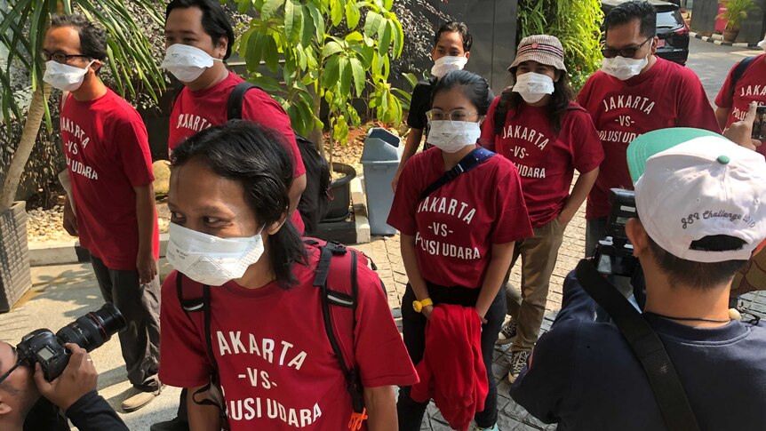People in red t-shirts and face masks file into a court room