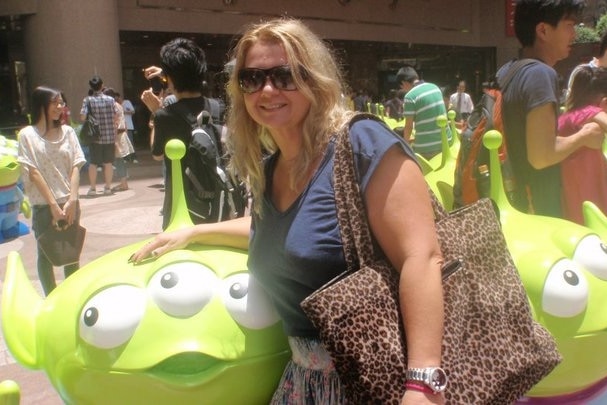 A woman with a large bag poses with a model of a cartoon alien