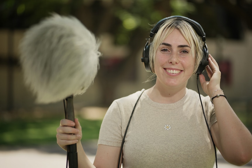 A blonde lady smiles as she holds a fluffy microphone.