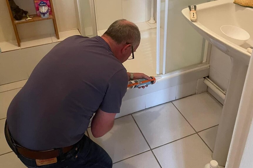 David Roberts kneeling by the shower applying a product to tiles. 