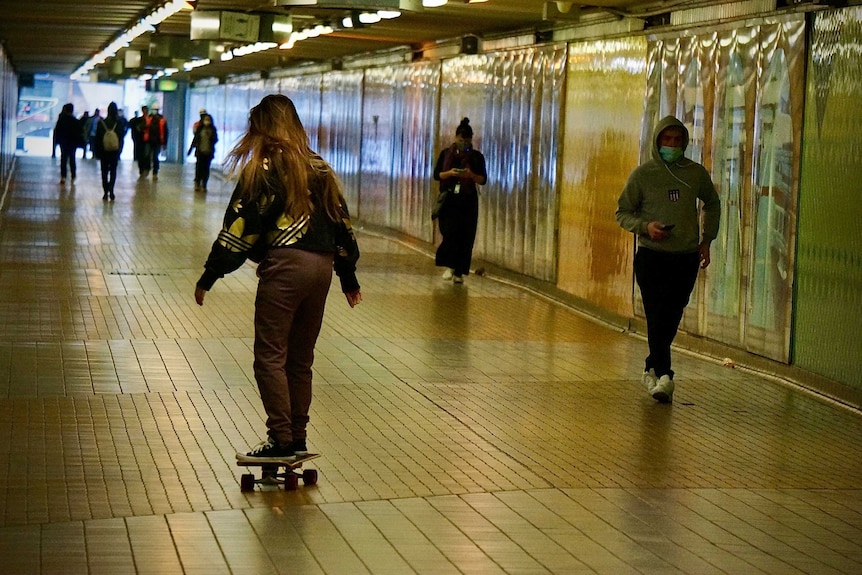 People wearing masks and a skateboarder in a pedestrian tunnel.