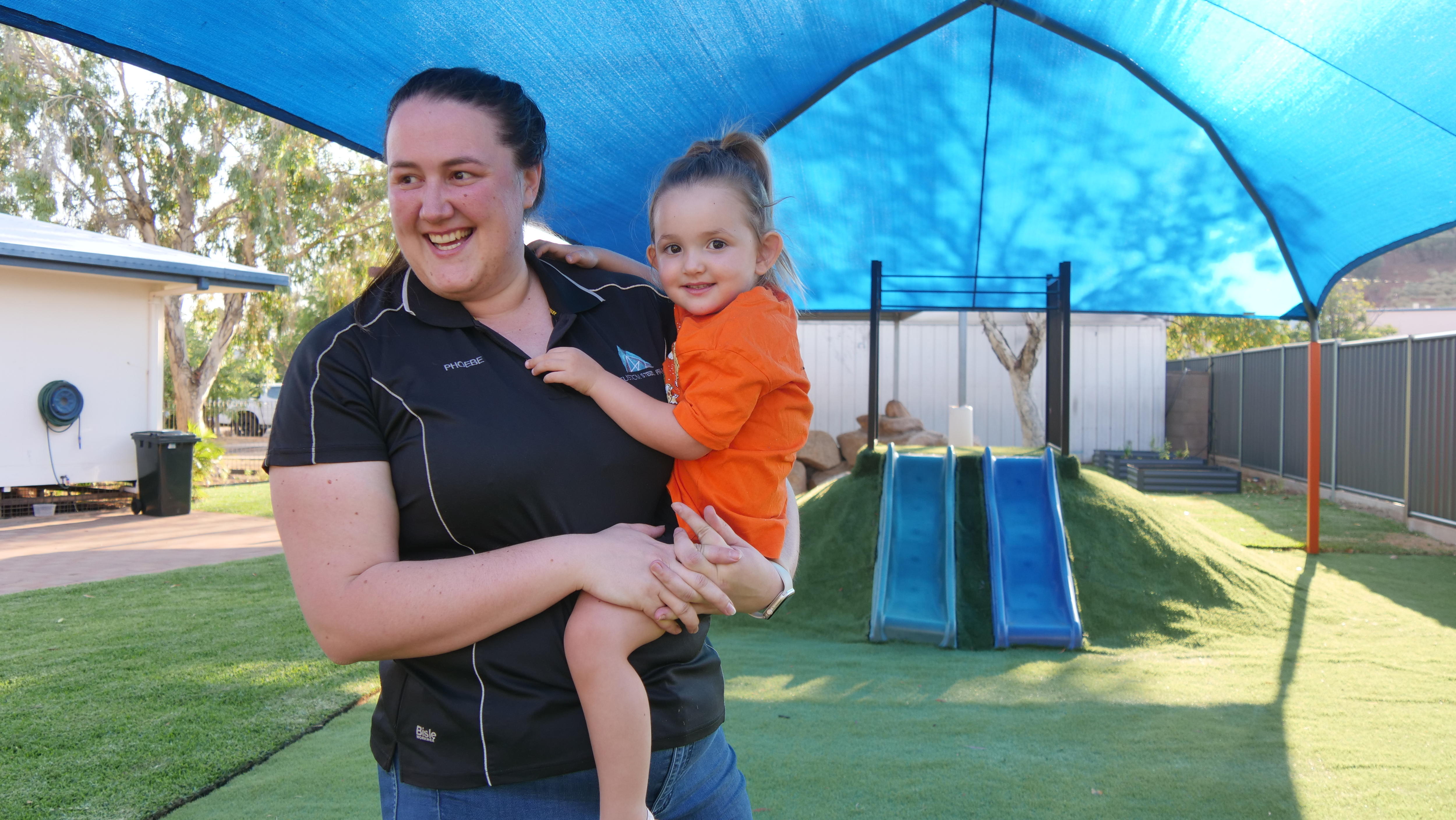 A woman holds her young daughter in a daycare playground