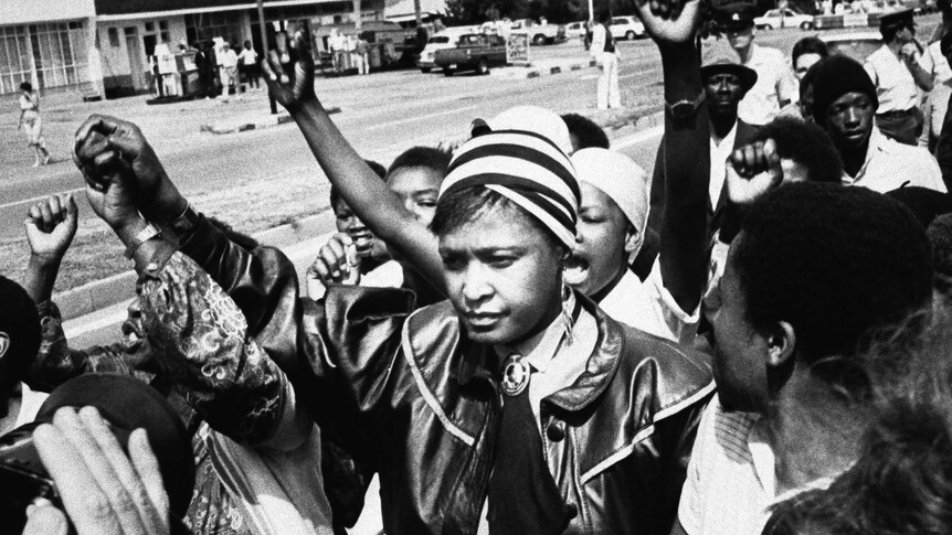 Winnie Mandela is cheered by supporters in 1986 in a black and white photo.