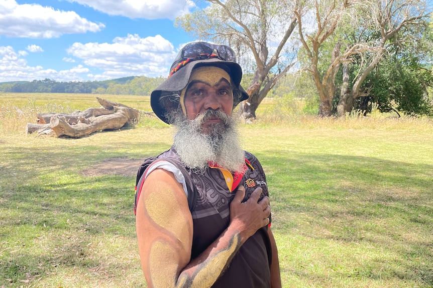 A man with a bushy beard, shows his ochre painted arm to the camera