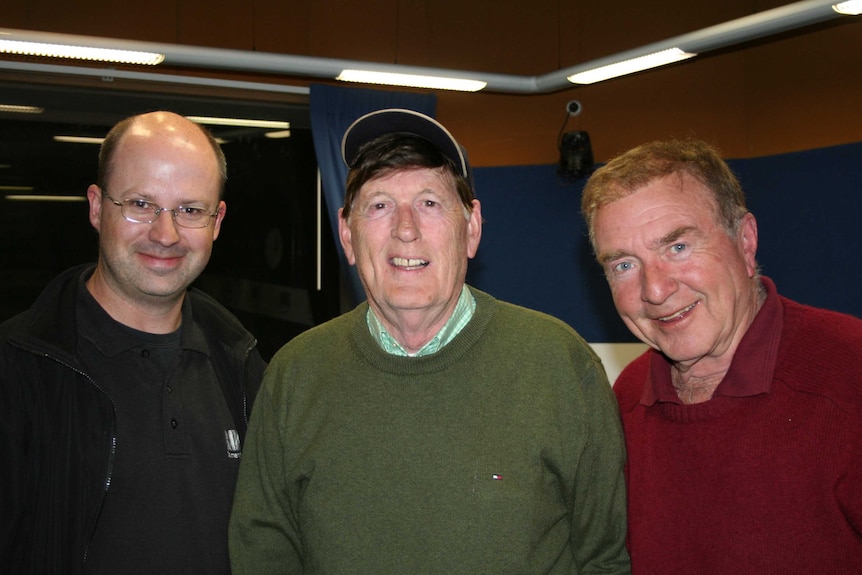 Three men stand together and smile.