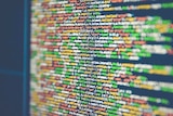 An image of a computer screen. Over a black background, multi-coloured rows of source code come into and out of focus