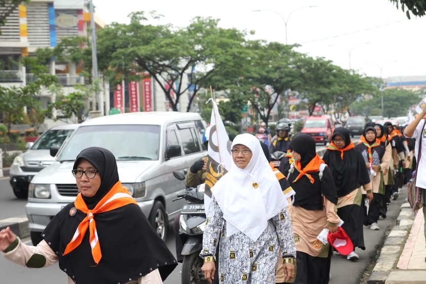 Women in black and white hijabs march down the street in Indonesia.