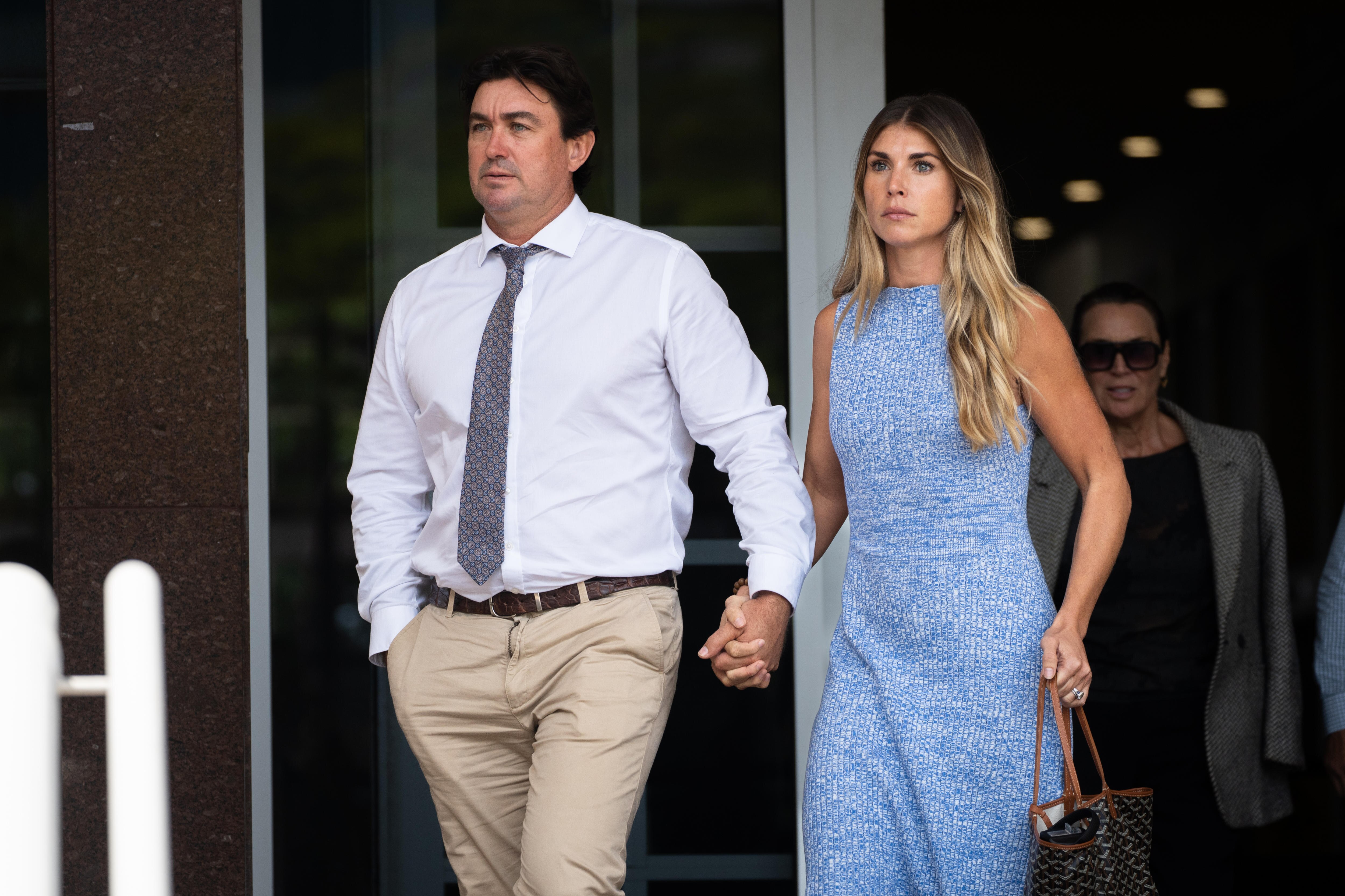A man in white shirt and tie and a woman in a blue dress walking holding hands.