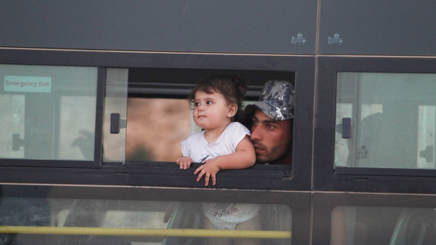 A man holds his toder up to see out the window of an evacuation bus in Lebanon