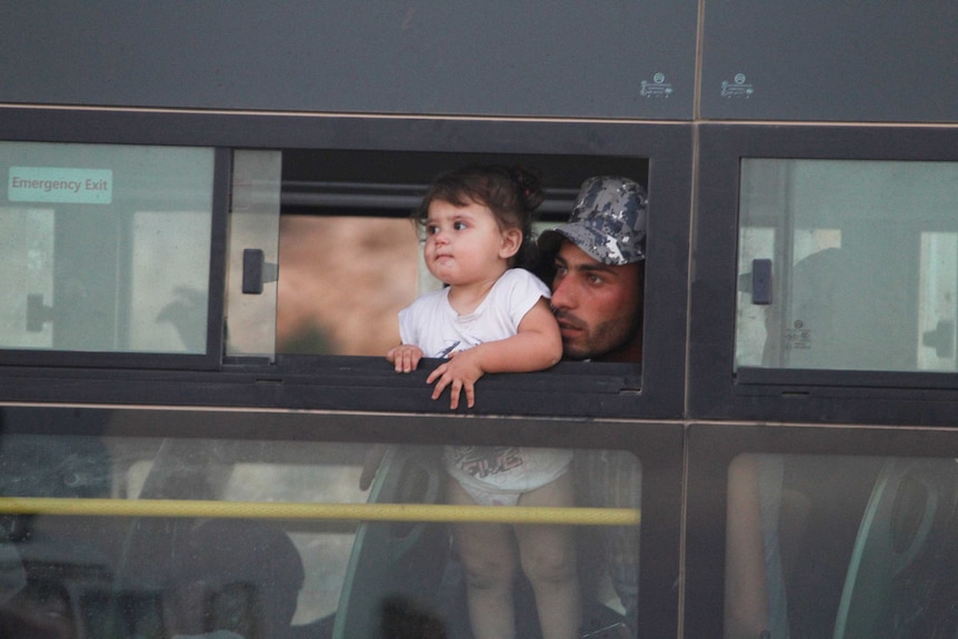 A man holds his toder up to see out the window of an evacuation bus in Lebanon