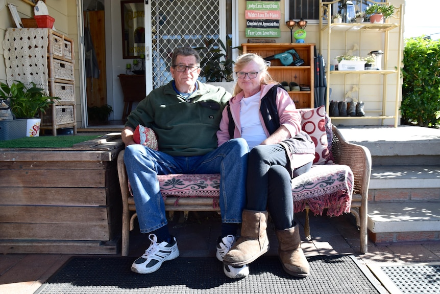 A man and woman sit on a chair outside in a yard.