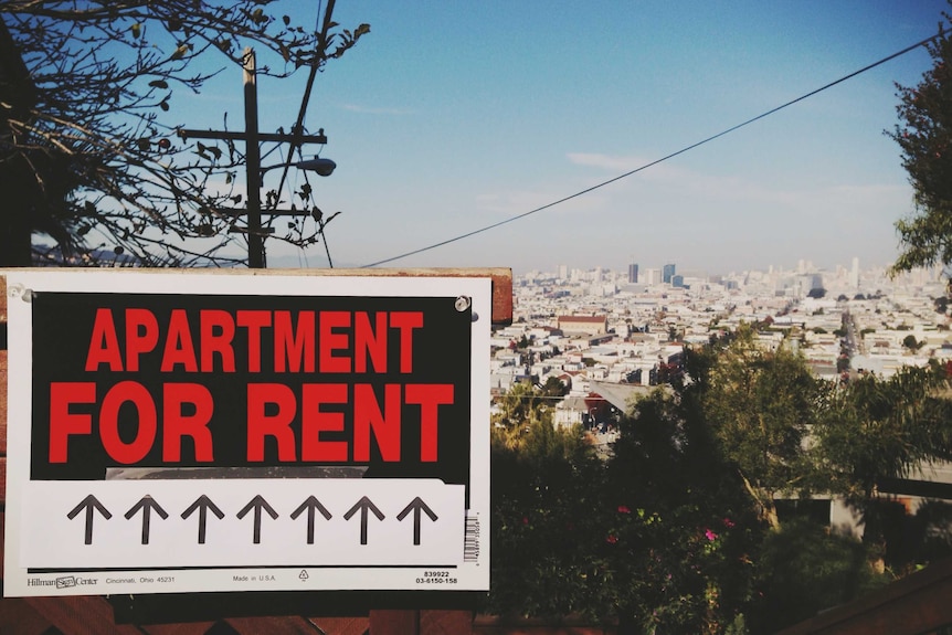 A sign reading 'For Rent' overlooks a big city.