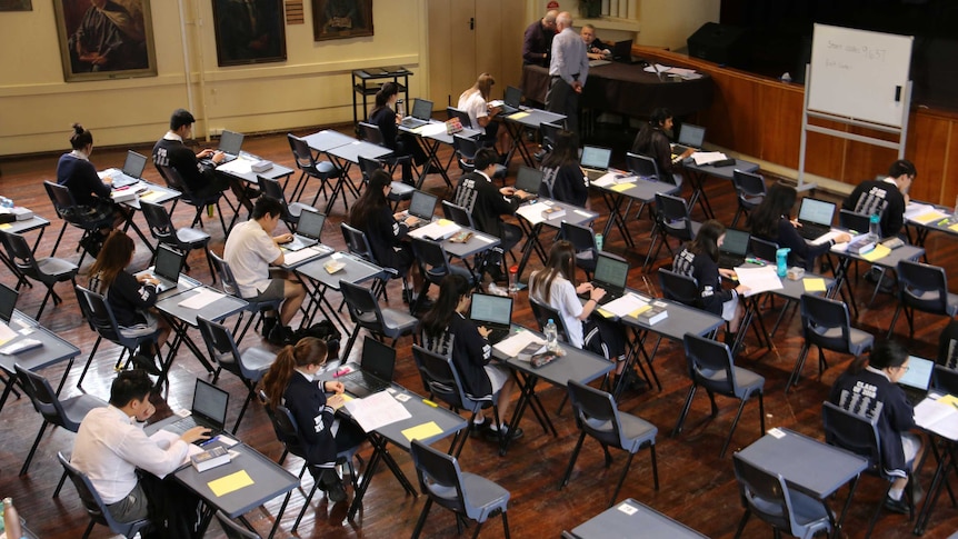 Students sit at desks completing their exam on lap tops.