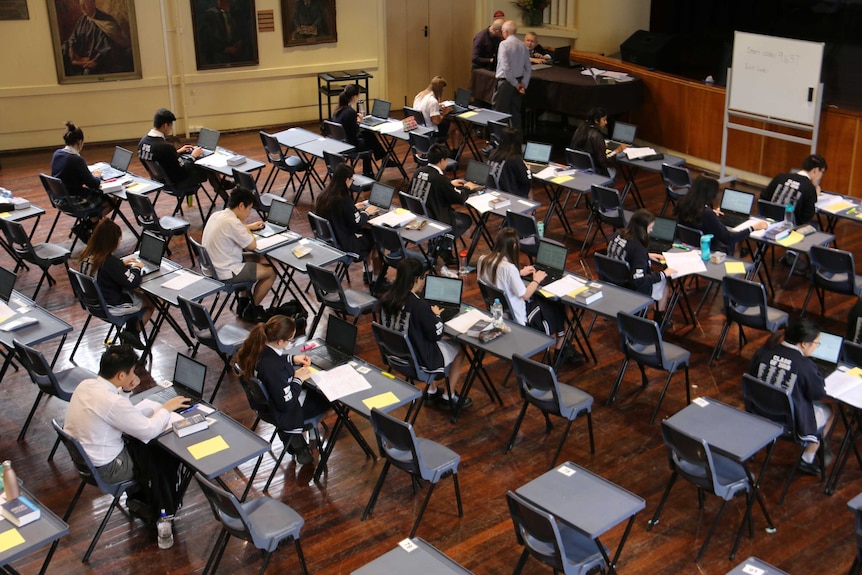 Students sit at desks completing their exam on lap tops.