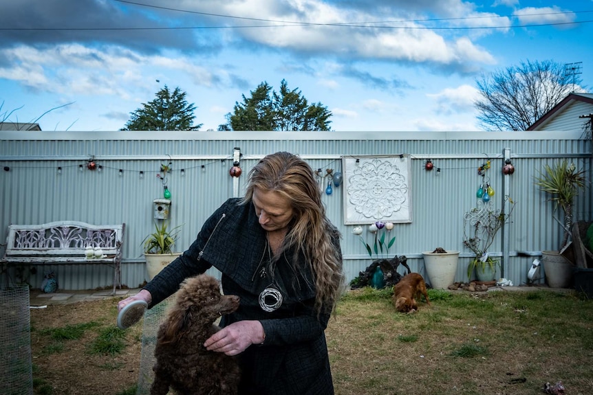 Donna stands in her backyard and brushes a poodle.