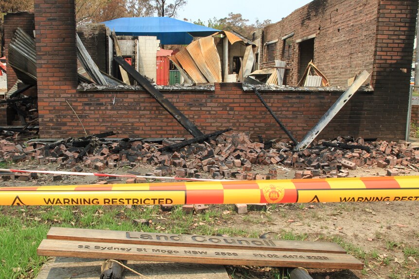 Burnt out brick office surrounded by rubble with Land Council sign and warning tape in foreground
