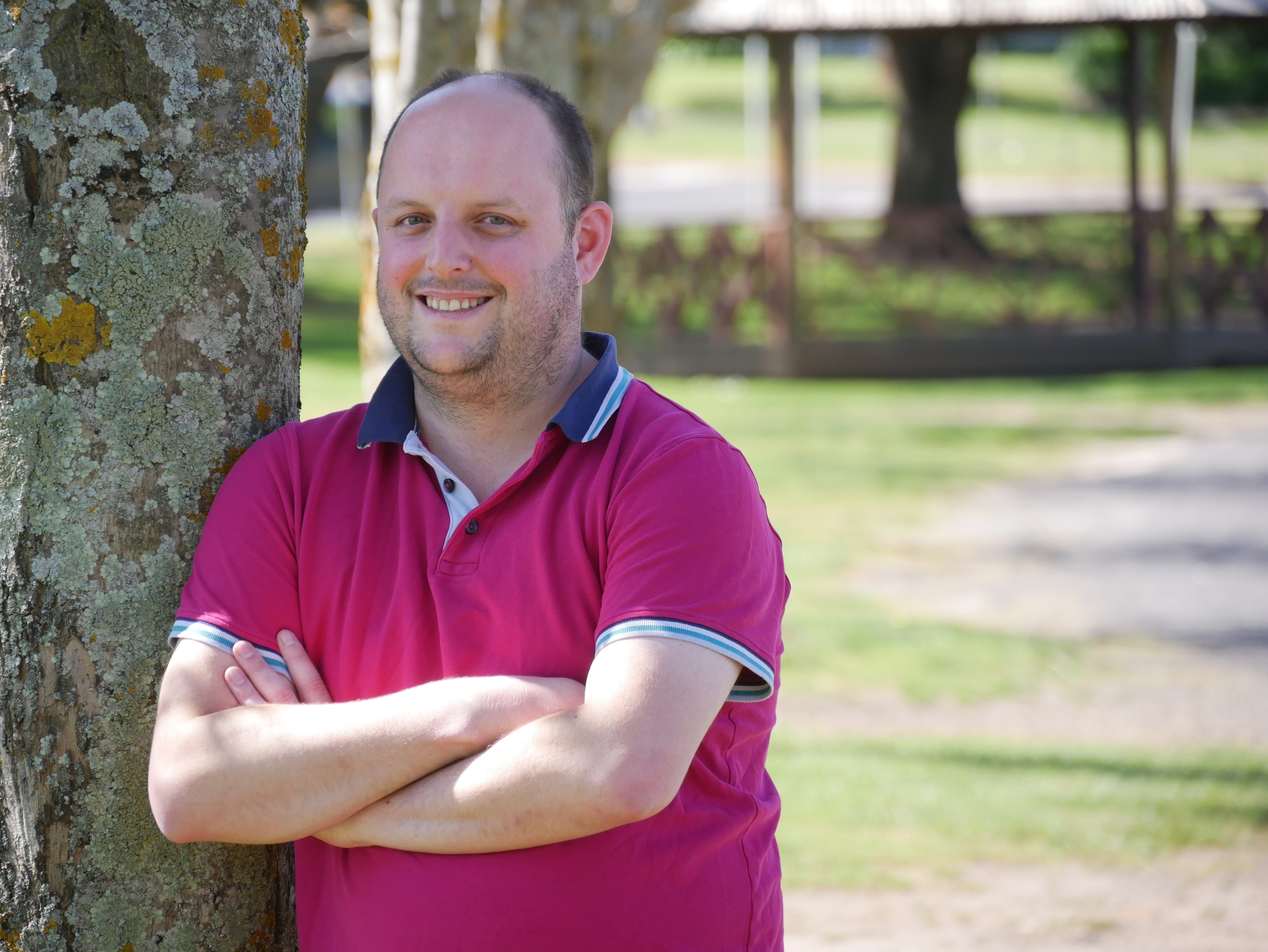 A man wearing a pink shirt leaning against a tree. 