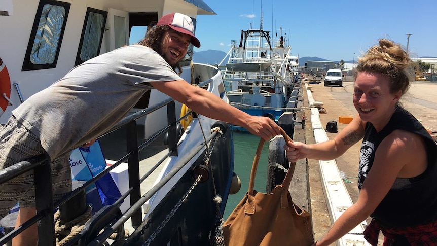 A trawler deckhand passes a bag to a female workmate standing on the wharf in Cairns