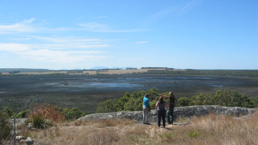 Wide shot of three people standing near a rocky outcrop overlooking wetlands and arid ranges