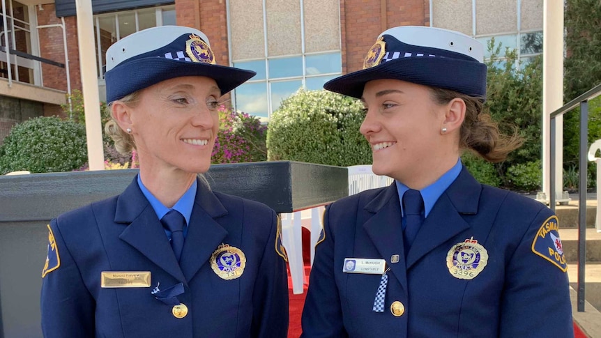 Two women in police uniforms smile at each other