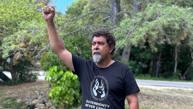 An Indigeous man with his fist in the air stands next to a creek