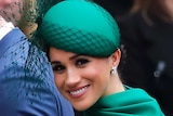 Britain's Prince Harry, wearing a suit and tie, and Meghan in a green dress walk together as Meghan looks toward the camera.