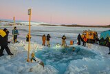 Antarctic expeditioners gather around a waterhole cut out of sea ice