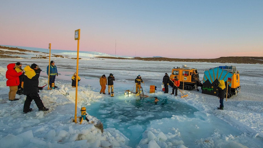 Antarctic expeditioners gather around a waterhole cut out of sea ice