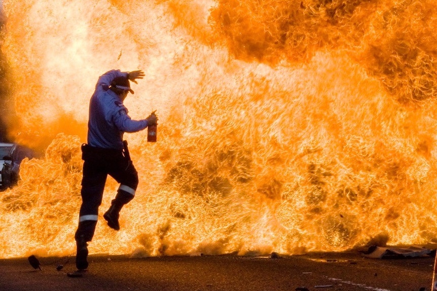 an actor in a police uniform in the foreground with a huge fireball explosion in the background