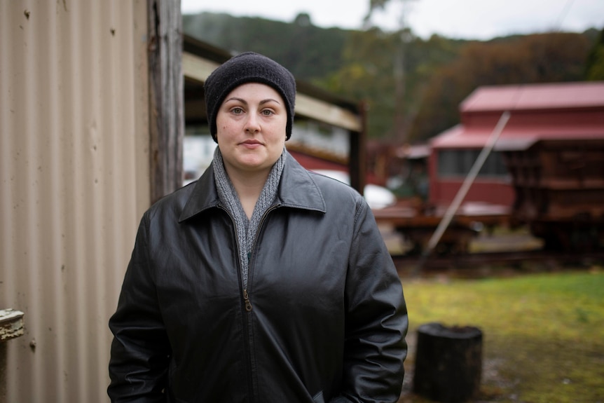 A woman wearing a black jacket looks seriously at the camera.