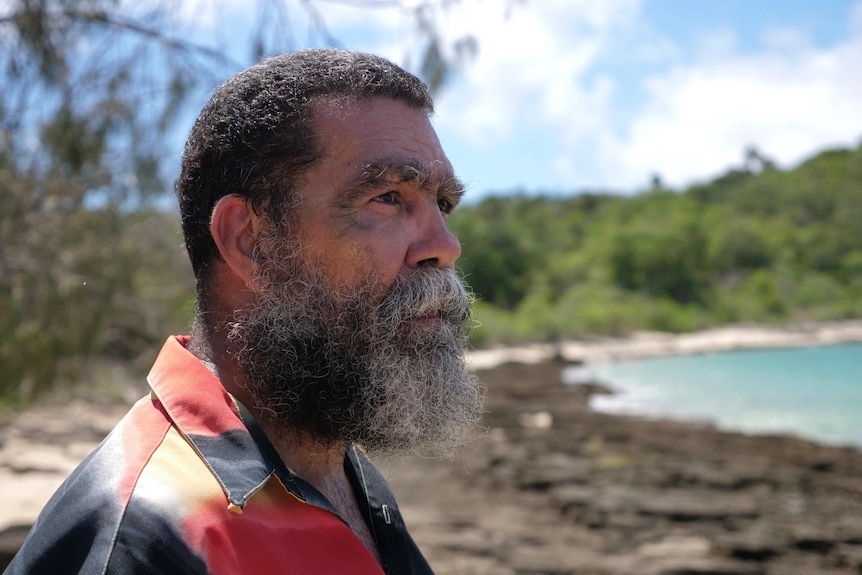 Close up shot of an Indigenous man standing on a beach looking out at the ocean