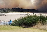 People watch a bushfire from a distance.