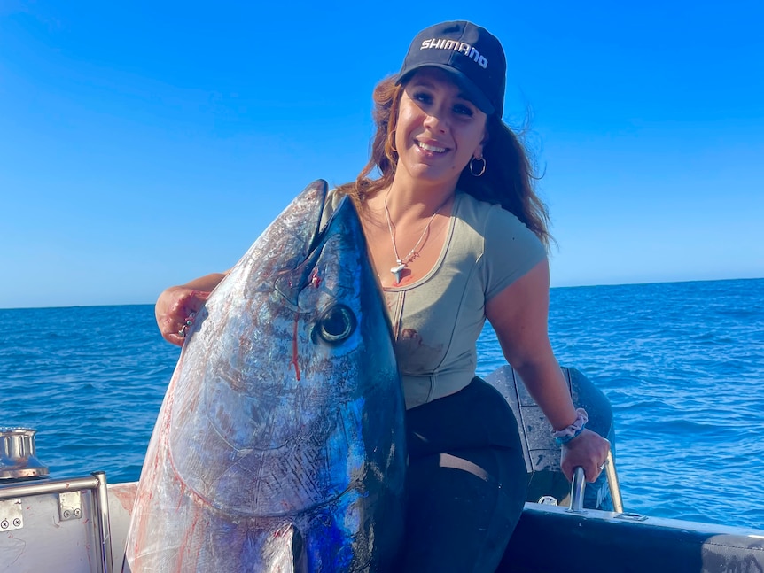 A woman on a boat holds up a big tuna with its tail missing