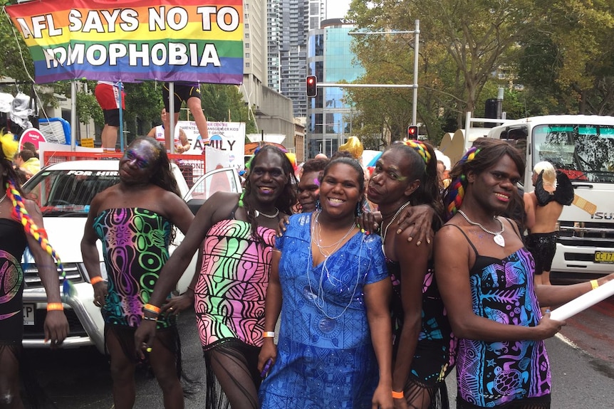 Sistagirls surrounded by rainbow flags and traffic on a busy city street