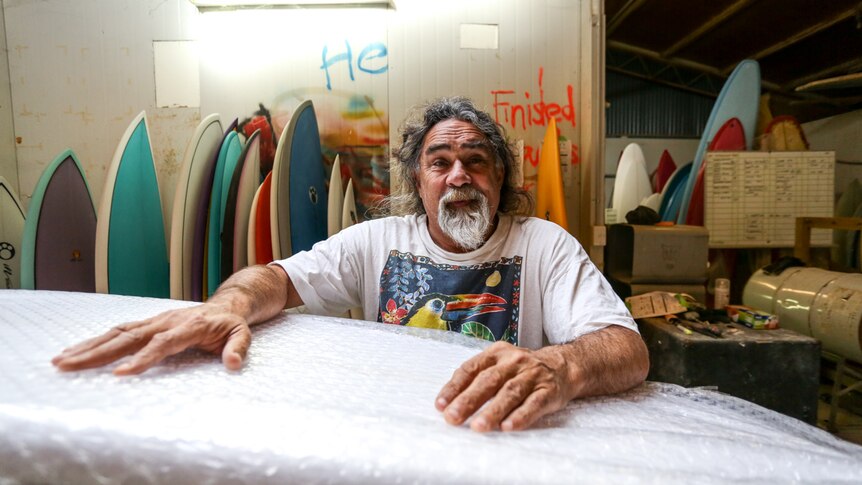 Maurice Cole against a backdrop of surfboards and leaning on new ones.