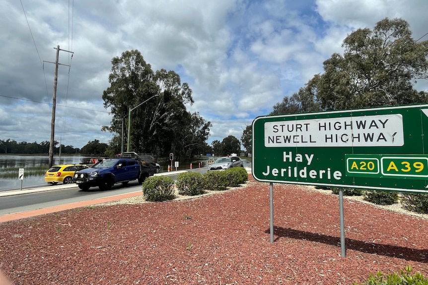 A highway intersection, with cars banked up, and a sign reading "Sturt Highway, Newell Highway, Hay, Jerilderie".