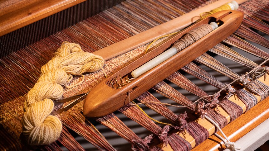A weaving loom with a shuttle and skein of alpaca yarn.