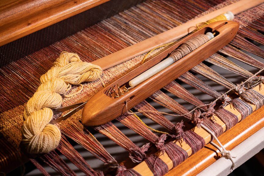 A weaving loom with a shuttle and skein of alpaca yarn.