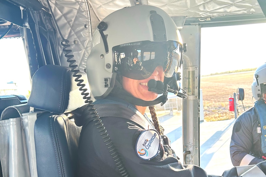A young helicopter rescue officer wearing a helmet, goggles and a seatbelt sitting in a helicopter ready for take off.