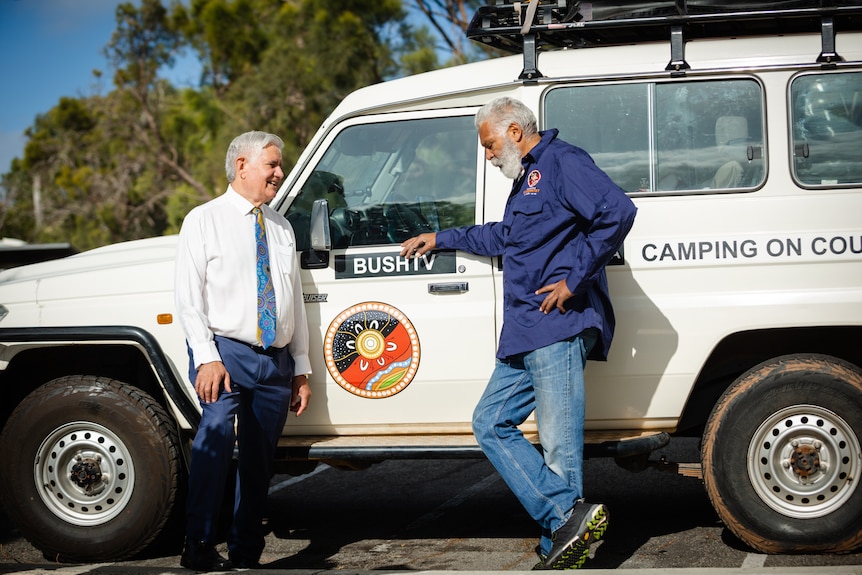 Ken Wyatt and Ernie Dingo stand next to a four-wheel drive having a conversation.