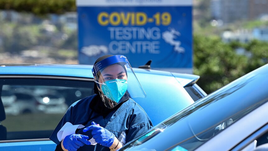 a healthcare worker outside a car with a covid 19 testing sign behind her