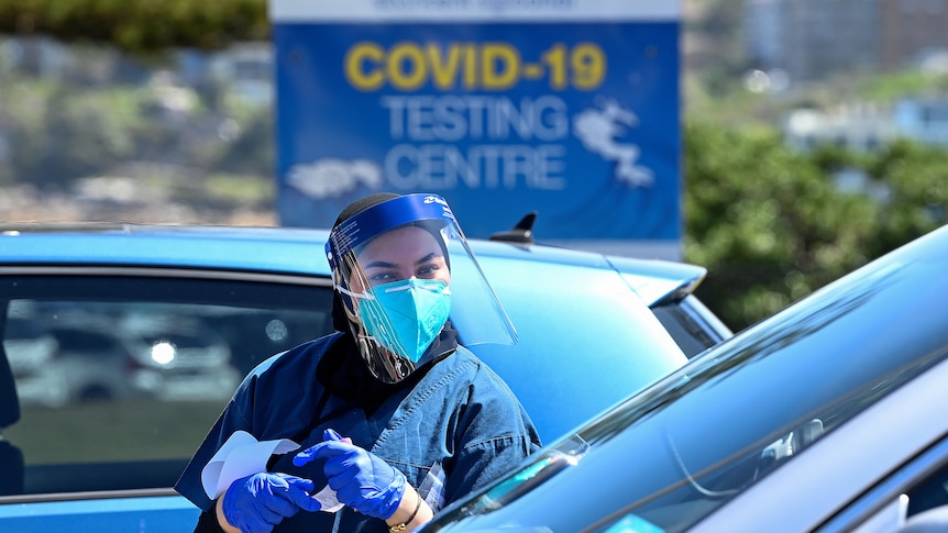 a healthcare worker outside a car with a covid 19 testing sign behind her