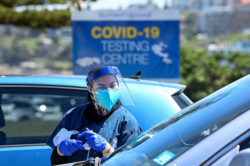 a healthcare worker outside a car with a covid 19 testing sign behind her