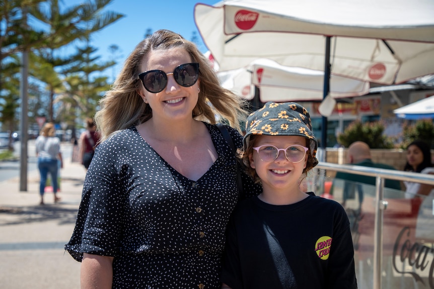 A woman with sunglasses hugs a child wearing a colourful bucket hat