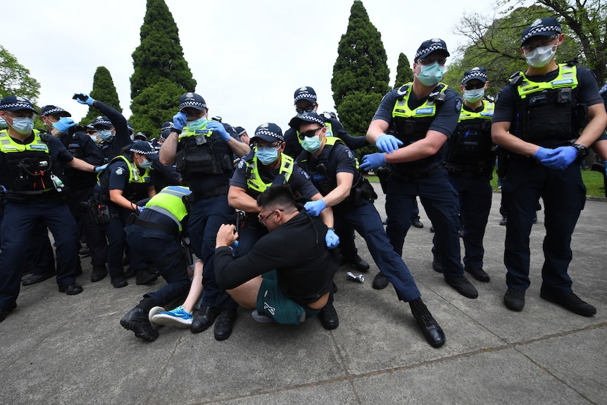 A group of masked police officers scuffle with a man who is on the ground.