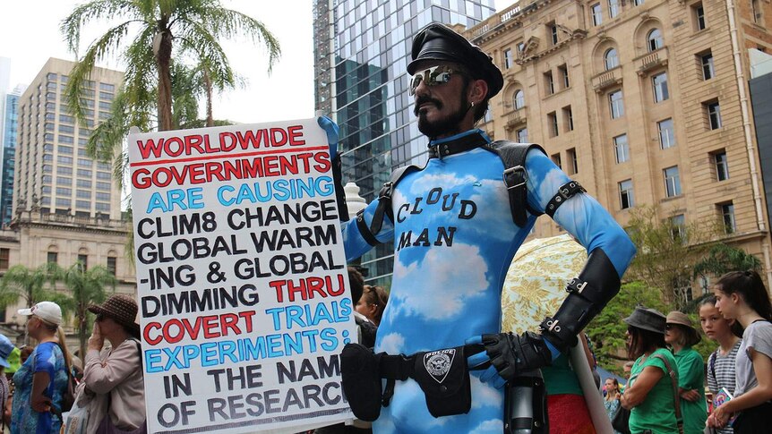 Man dressed in blue and white leotard with Cloud Man written on his chest, with a sign saying governments cause climate change
