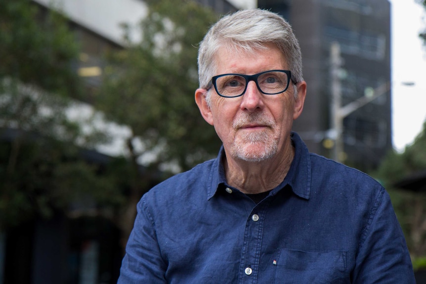 Quaker Tim Sowerbutts wears black glasses and a blue denim shirt. He sits in Surry Hills.