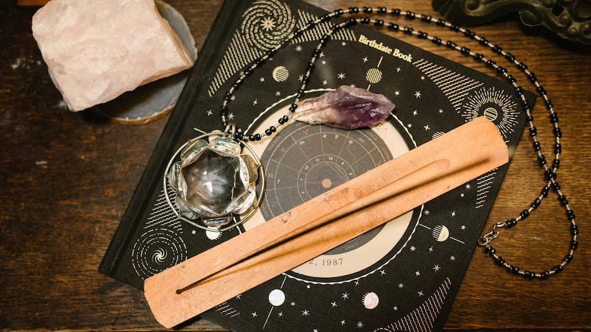 An incense stick and purple crystals sit on top of an astrology chart