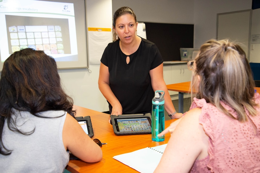 Two people sitting in a classroom setting with a woman in a black shirt holding a tablet computer