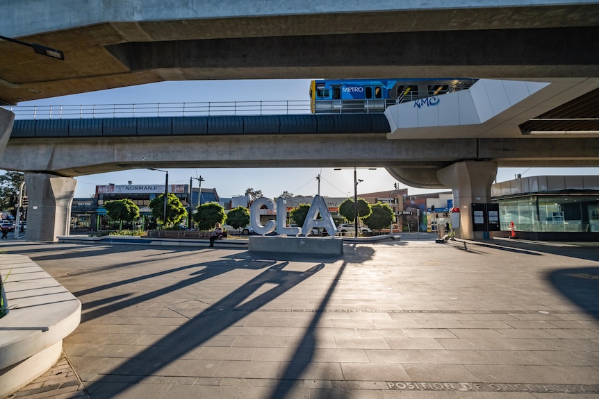 The letters CLA overlook concrete ground as a train moves on a railyway track overhead.